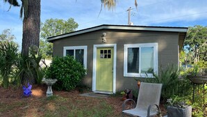 A small, single-story house with a green door and white-framed windows, surrounded by greenery and a bird sculpture. - Waterfront coastal cottage charm in delightful Port Royal (Port Royal)