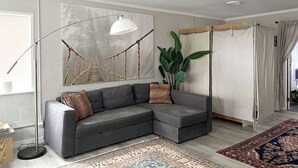 A modern living room with a grey sectional sofa, a floor lamp, a large abstract painting, a hanging plant, and a curtain divider. - Waterfront coastal cottage charm in delightful Port Royal (Port Royal)