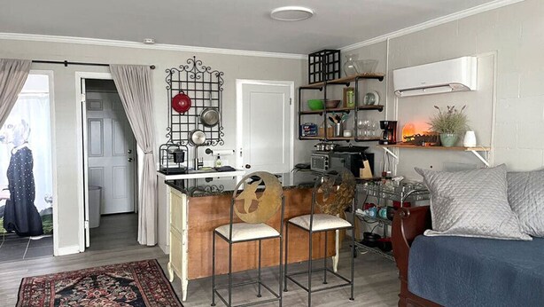 A compact living space with a kitchenette, a dining area with two stools, a bed with a blue cover, and a patterned rug. - Waterfront coastal cottage charm in delightful Port Royal (Port Royal)
