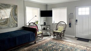A bedroom with a bed, two wicker chairs, a television, and a large abstract painting on the wall. - Waterfront coastal cottage charm in delightful Port Royal (Port Royal)