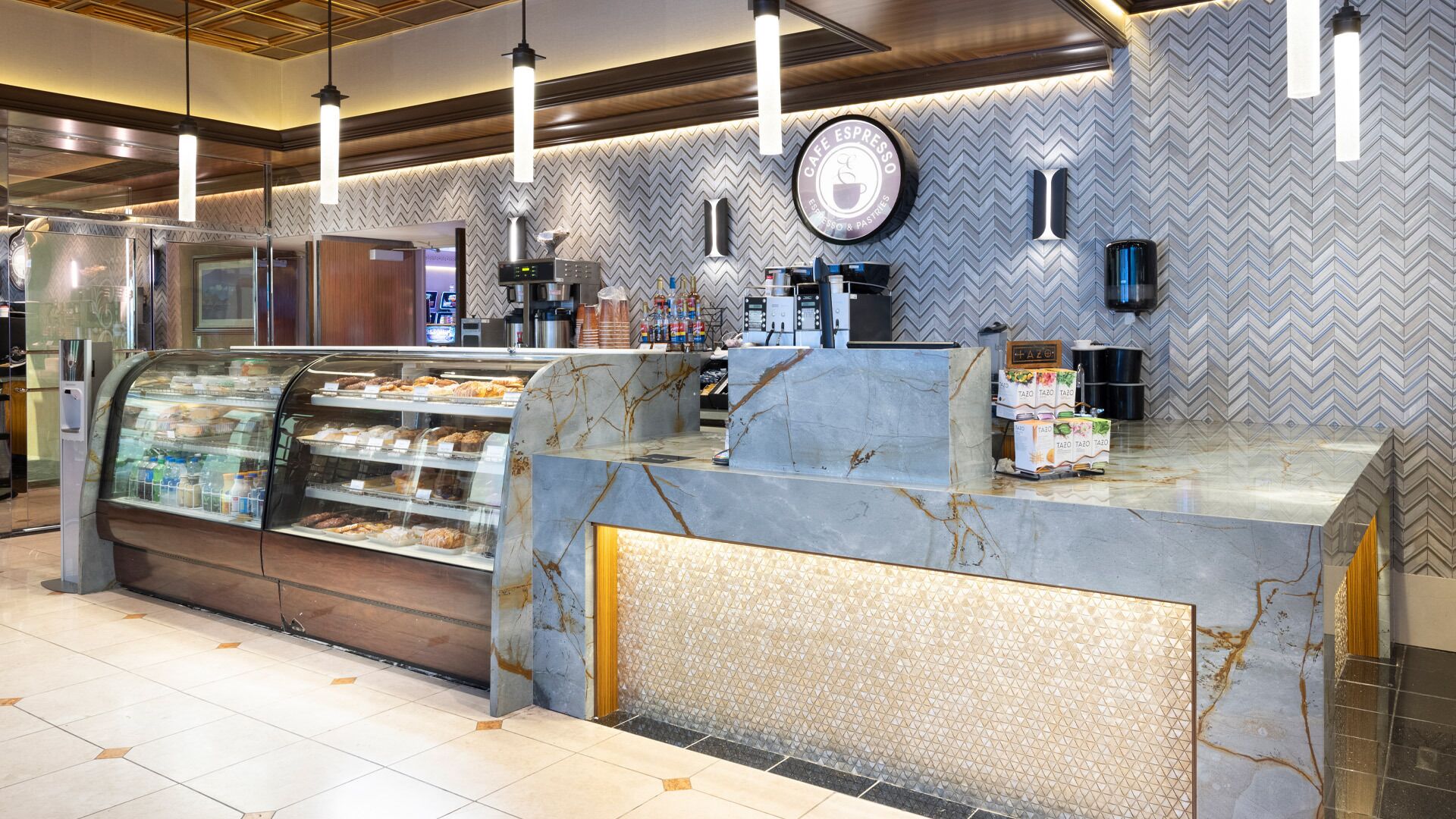 A cafe with a marble counter, espresso machines, and a display case with pastries.
