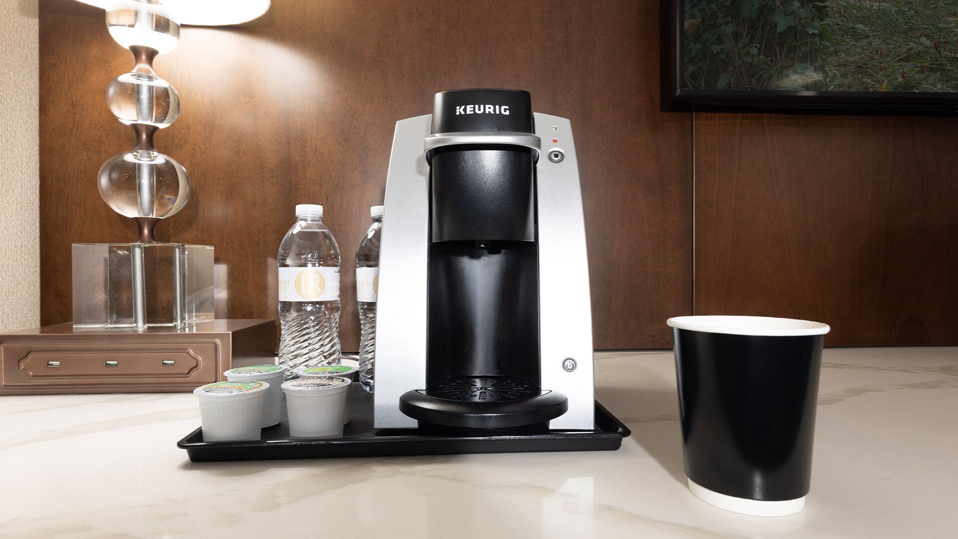 A Keurig coffee machine with a water bottle, two cups of coffee, and a black cup on a countertop.