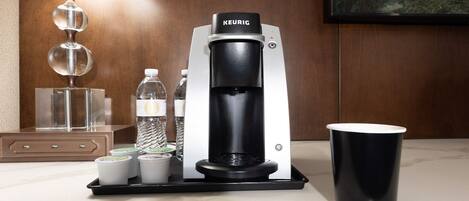 A Keurig coffee machine with a water bottle, two cups of coffee, and a black cup on a countertop.