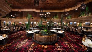 Un restaurante espacioso con barra central, varias mesas de comedor y una variedad de cactus y plantas.