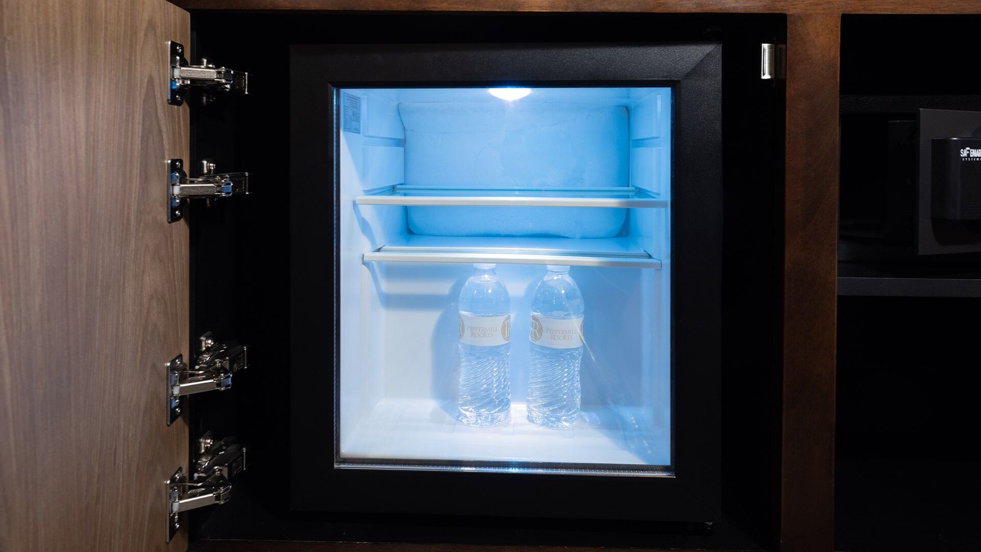 A refrigerator with a clear glass door, containing two bottles of water and a shelf.