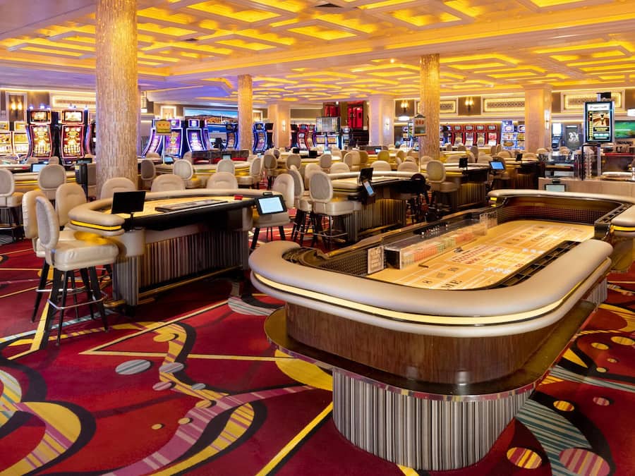 Ein Casino mit mehreren Spieltischen, Stühlen und Spielautomaten.
