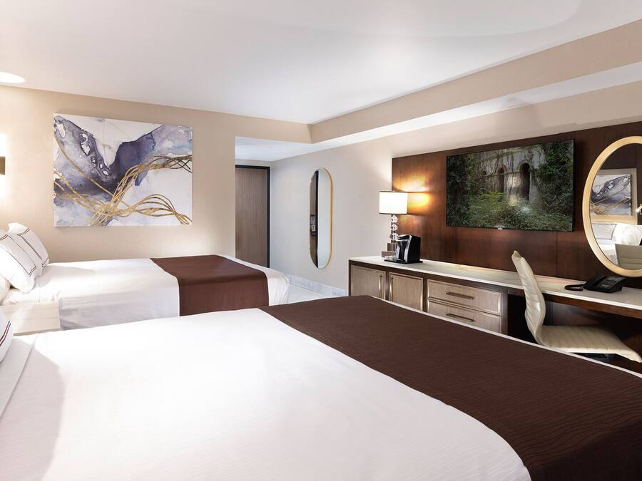 A hotel room with two beds, a desk, a chair, a large mirror, and artwork on the walls.