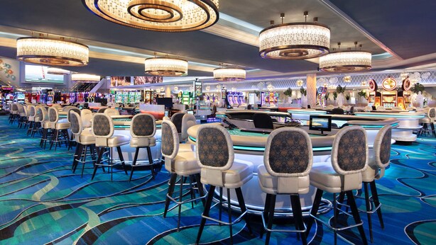 Un casino con numerosas mesas de juego, sillas y candelabros colgantes.