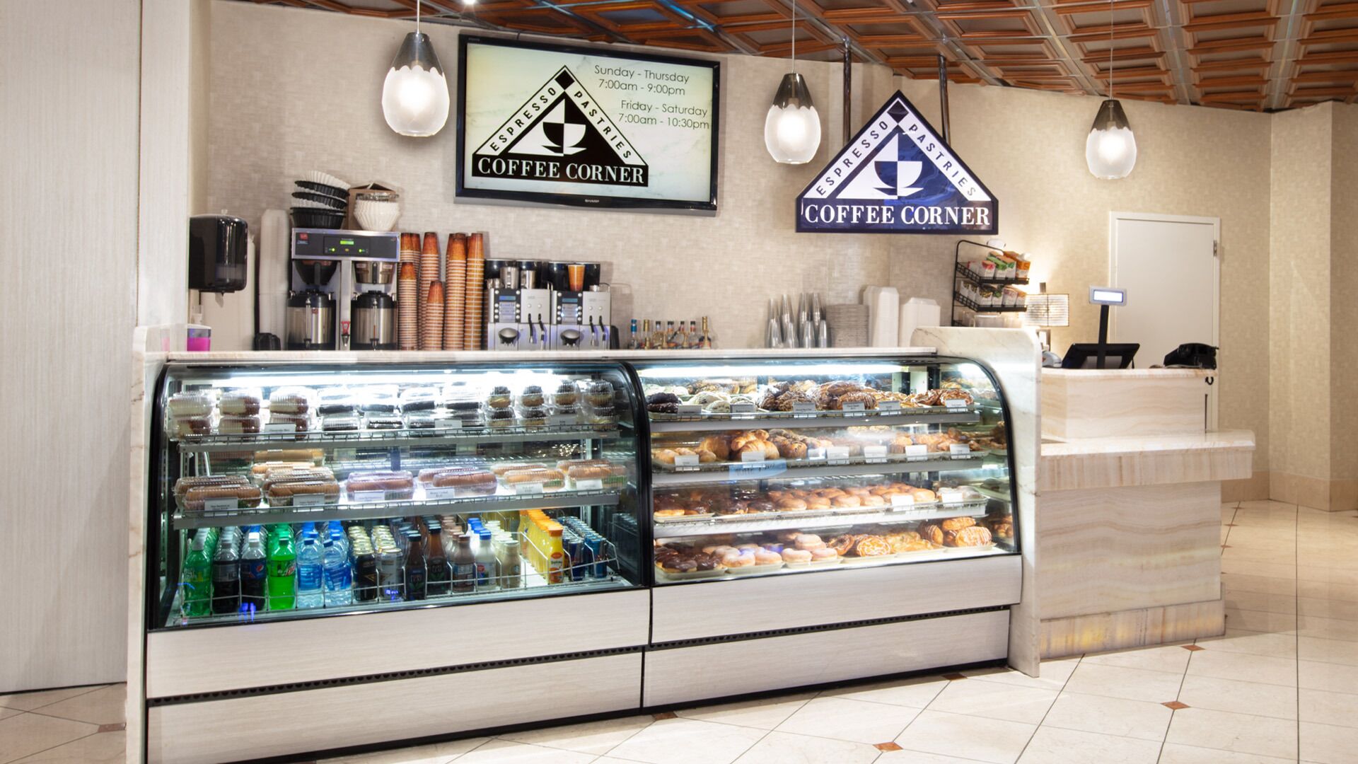Un café où l’on peut admirer une vitrine remplie de pâtisseries et où se trouve un comptoir avec une caisse enregistreuse.