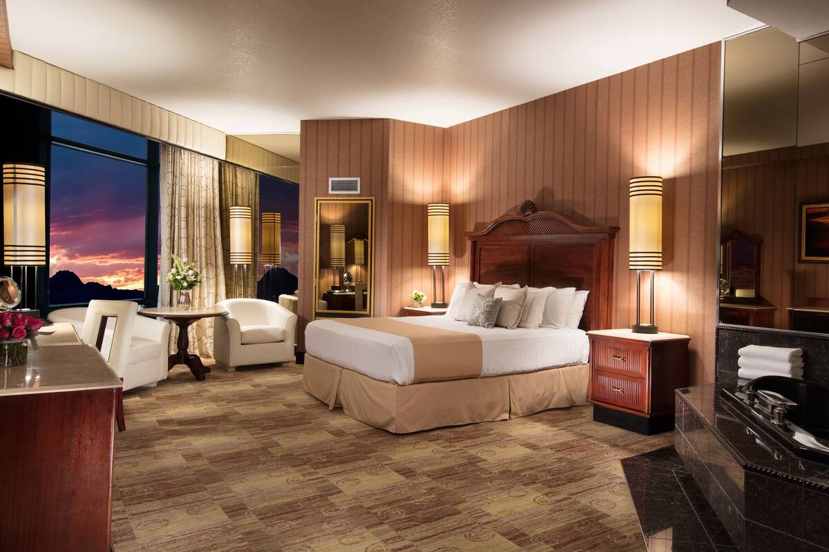 Habitación de hotel con una cama grande, un escritorio con silla, un tocador con espejo y una bañera.