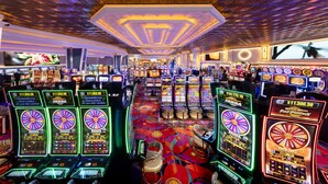 Een casino met meerdere gokkasten, een kamerbreed tapijt met een patroon en een plafond met een geometrisch ontwerp.