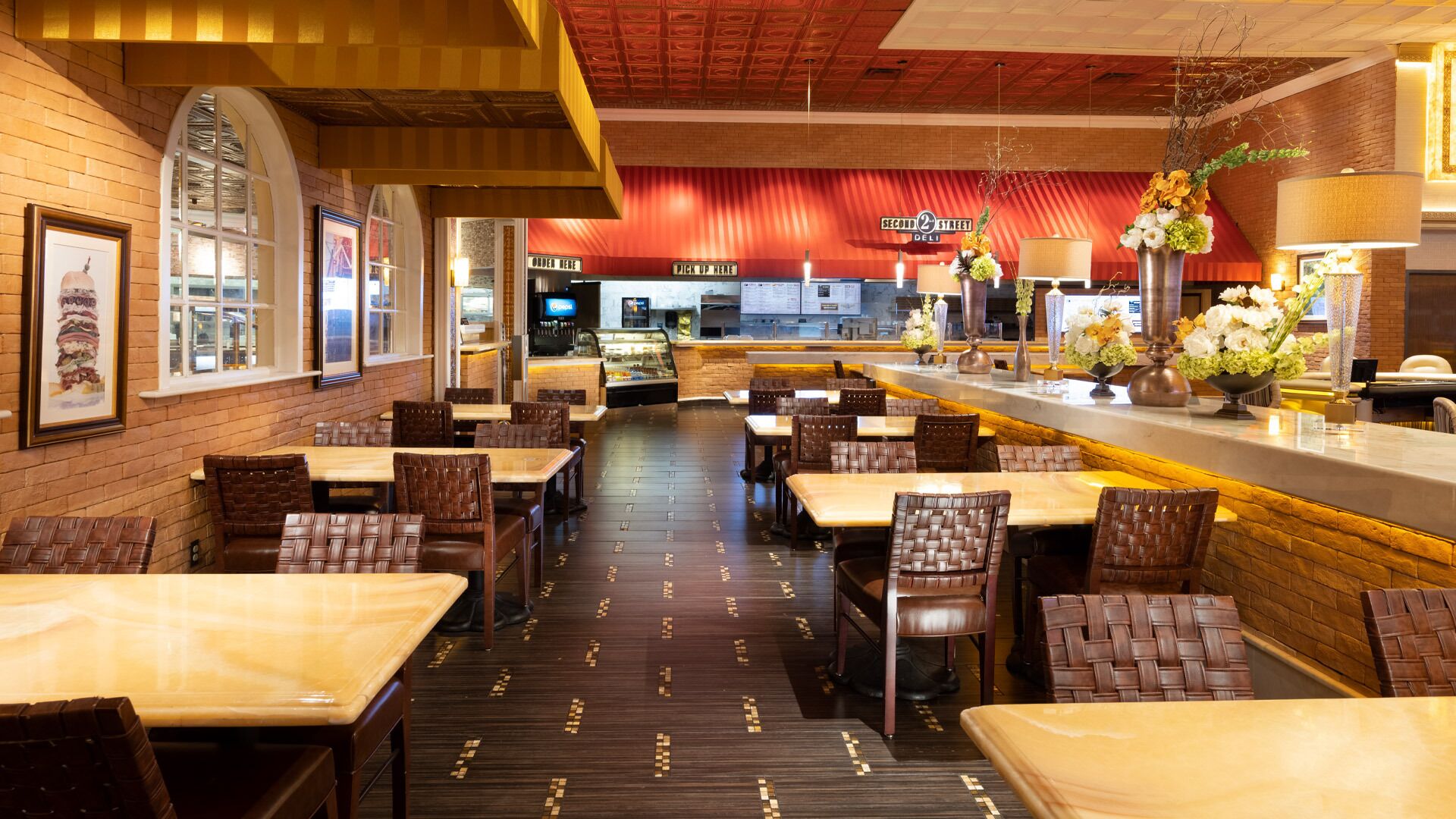 A restaurant with brick walls, wooden ceiling, and a counter with flowers. Tables and chairs are arranged for dining.