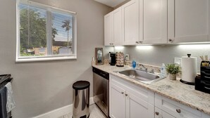 A kitchen with white cabinets, a stainless steel sink, and a window with blinds.