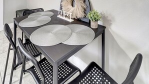 A dining area with a dark wooden table, black chairs, and a wall-mounted painting of potted plants.