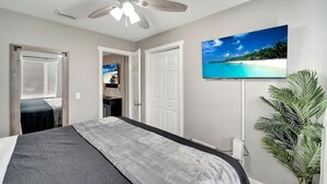 A bedroom with a bed, a ceiling fan, a TV on the wall, and a door leading to another room.