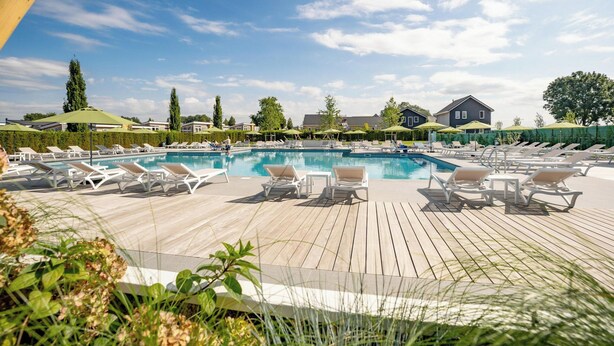 A pool area with lounge chairs and umbrellas, surrounded by greenery and buildings. - Holiday Home With gas Fireplace & Bath (Bemelen)