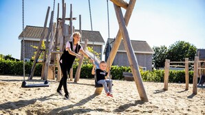 A playground with swings and a slide, surrounded by sand and wooden structures. - Holiday Home With gas Fireplace & Bath (Bemelen)