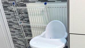 Valkoinen syöttötuoli, jossa on pöytätaso, on sijoitettu keittiöön. Keittiössä on marmorilattia ja taustalla valkoinen patteri.