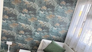 Una habitación con una cama, una mesita blanca pequeña y un almohadón verde, además de una pared con textura.