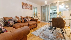 Una sala de estar moderna con un sofá de cuero marrón, una mesa de centro de vidrio y una zona de comedor con una silla.