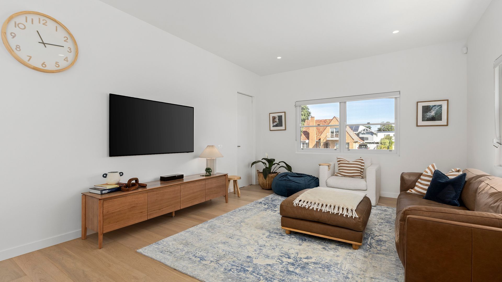 A modern living room with a flat-screen TV, wooden console, sofa, and a large window offering a view of houses.