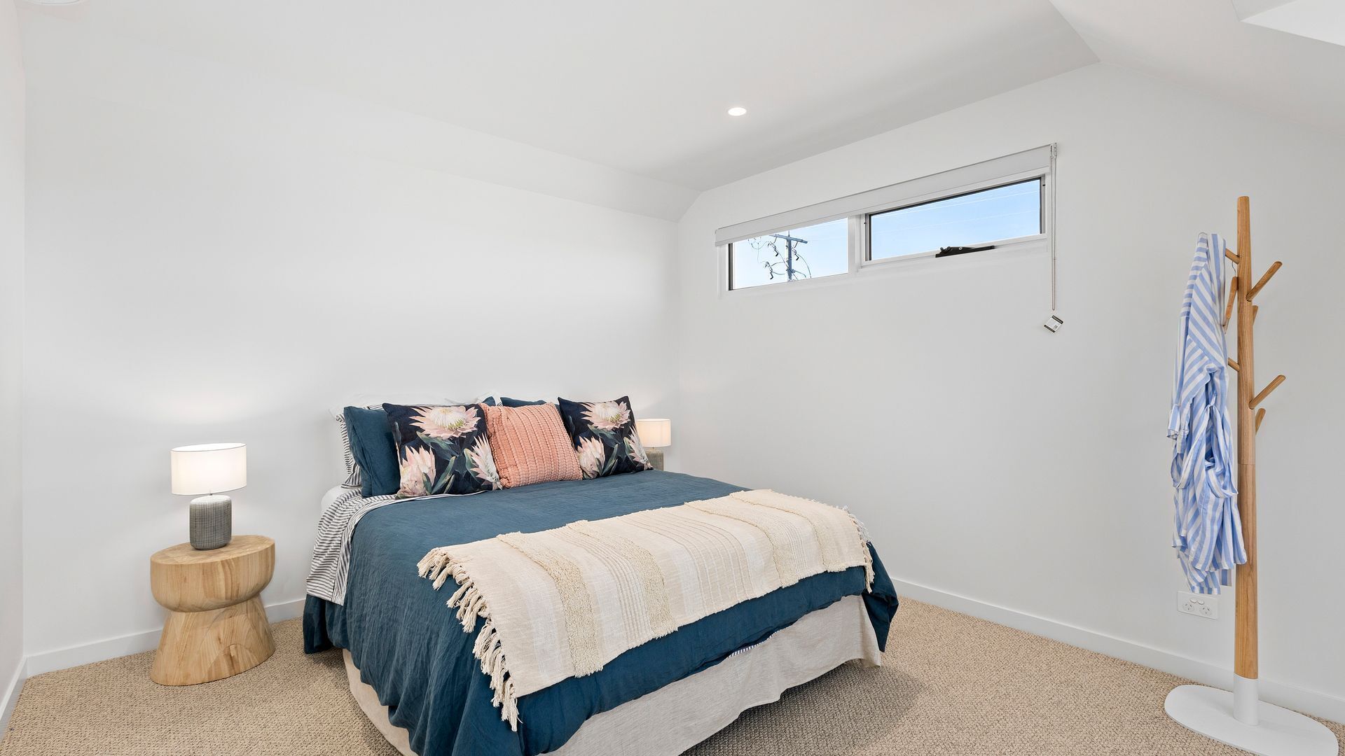 Un dormitorio con cama, mesita de noche, lámpara, ventana y perchero.