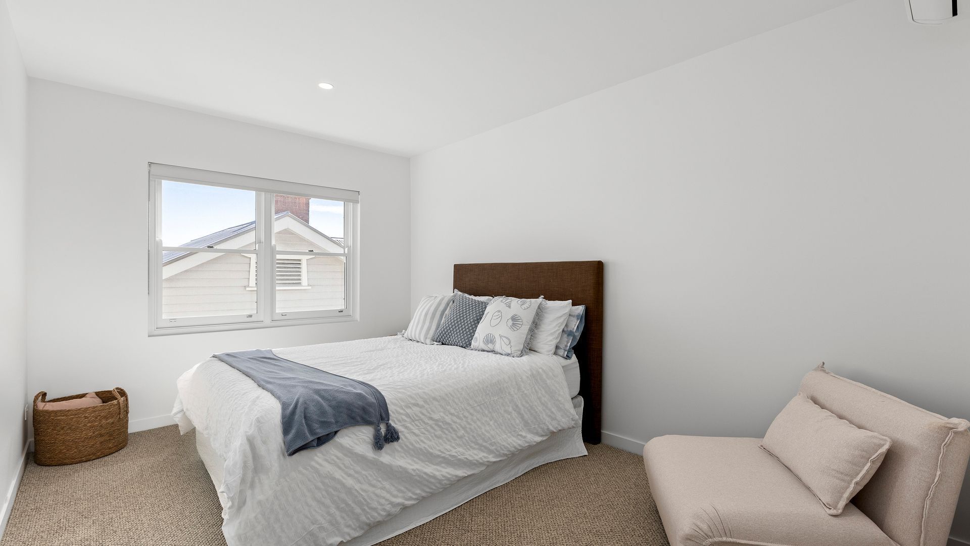 A bedroom with a bed, a window, a chair, and a small basket.
