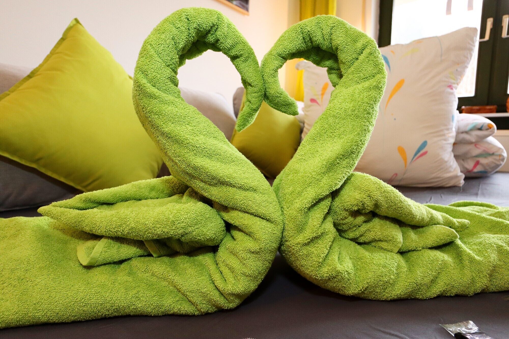 Un lit avec une serviette verte disposée en forme de cœur.