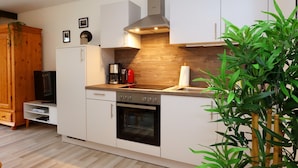 A modern kitchen with white cabinets, a stainless steel range hood, a built-in oven, and a coffee maker.