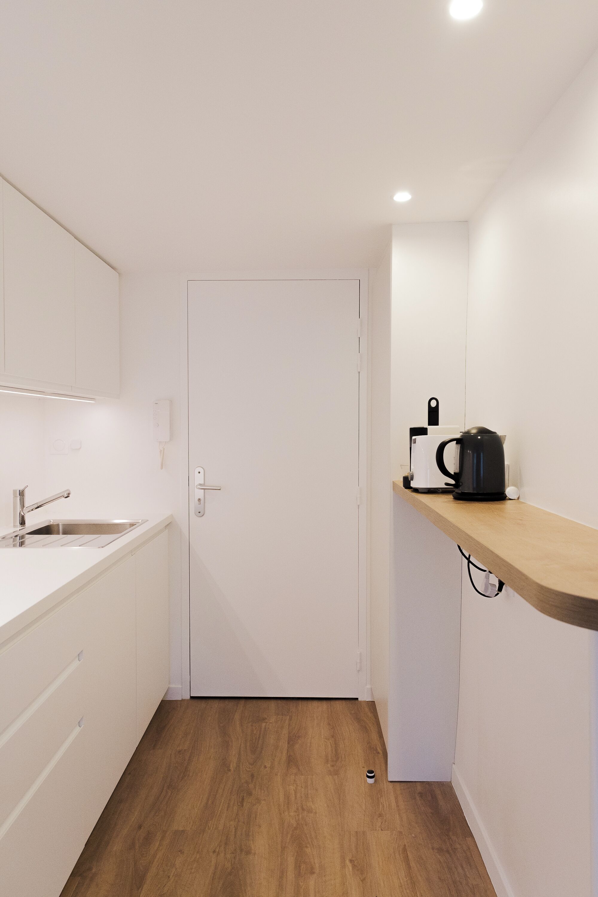A small, modern kitchen with white cabinets, a wooden countertop, and a coffee machine.