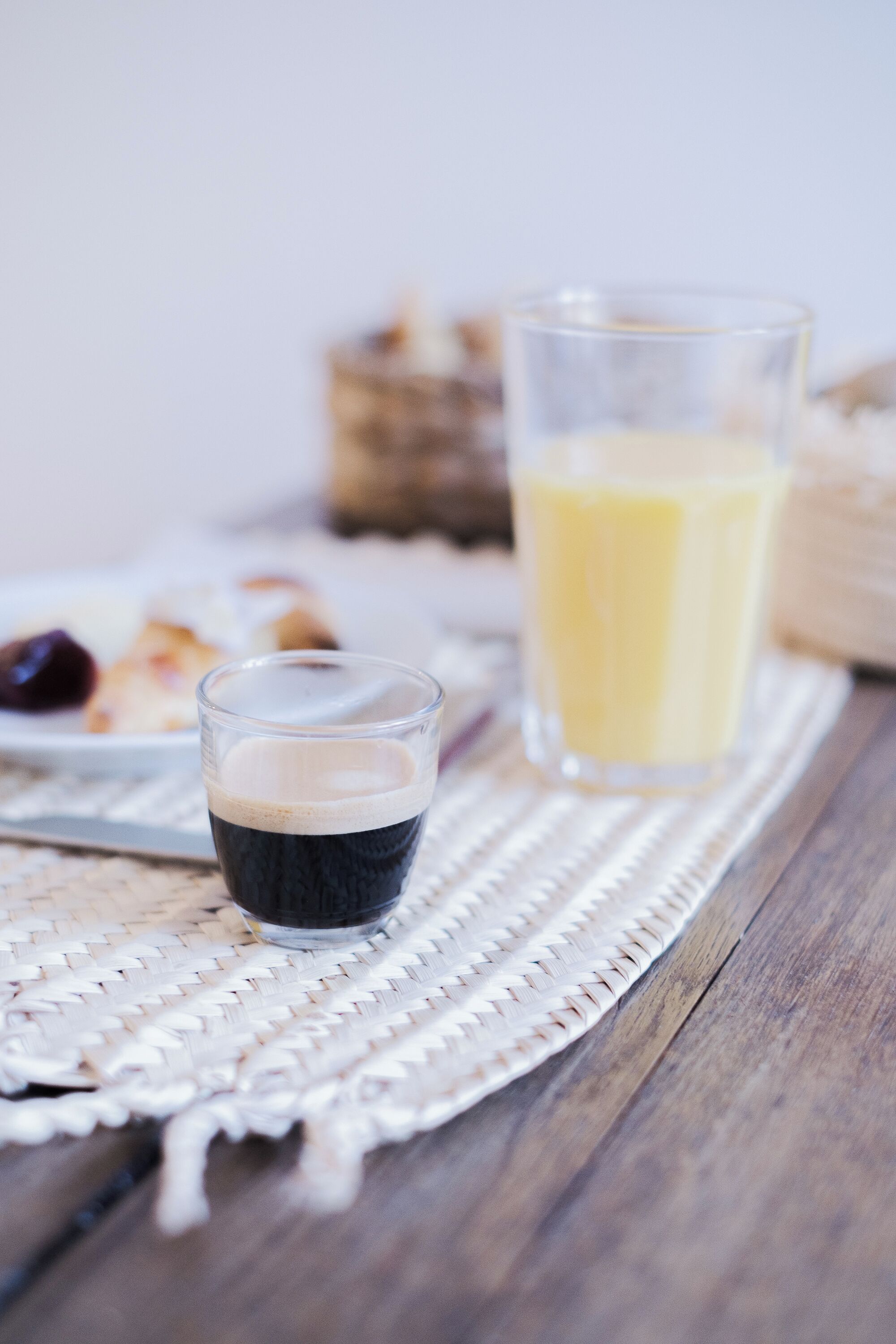 Un vaso de líquido oscuro, posiblemente café, y un vaso de líquido amarillo, seguramente jugo, sobre un posavasos tejido.