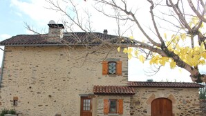 Un bâtiment en pierre avec un toit en tuiles, des volets en bois et une grande porte en bois.