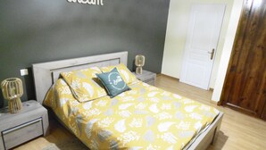 Une chambre à coucher comprenant un lit, des tables de chevet, une lampe de chevet et une lampe fixée au mur, ainsi qu’une porte.
