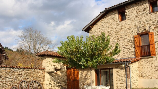 Un bâtiment en pierre avec un toit en tuiles, une porte en bois et une petite terrasse avec une table et des chaises.