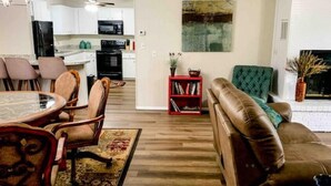 A modern living room with a brown leather sofa, a dining table with chairs, a red bookshelf, and a kitchen in the background. - ★Clean&Fresh★3BR/2BA★EZ access to S LBK/S Loop 289 (Lubbock)