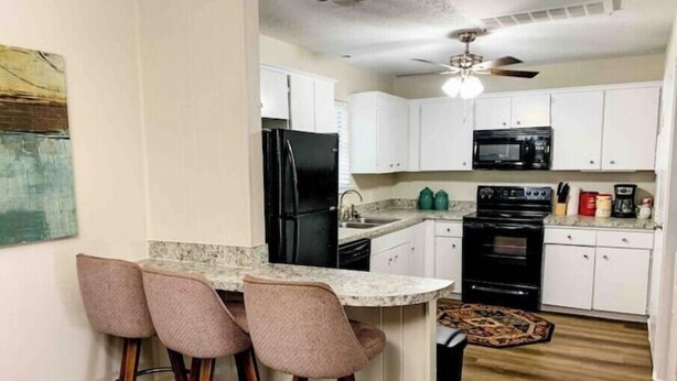 A kitchen with white cabinets, a black refrigerator, a microwave, and a stove. There are three bar stools with wooden legs and a marble countertop. - ★Clean&Fresh★3BR/2BA★EZ access to S LBK/S Loop 289 (Lubbock)