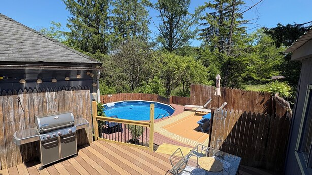 A backyard with a swimming pool, a barbecue grill, and a deck with outdoor furniture.