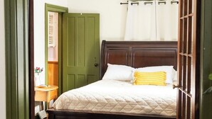 A bedroom with a bed, a green door, a white curtain, and a wooden headboard.