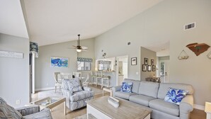 Un salon spacieux avec un canapé gris, des fauteuils à motifs, une table basse et un ventilateur de plafond.