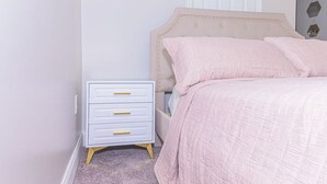 Een slaapkamer met een bed, een nachtkastje met lades en een deur op de achtergrond.