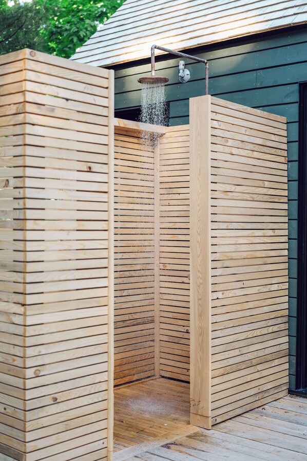 Un cerramiento para ducha exterior de madera con cabezal de ducha tipo lluvia.