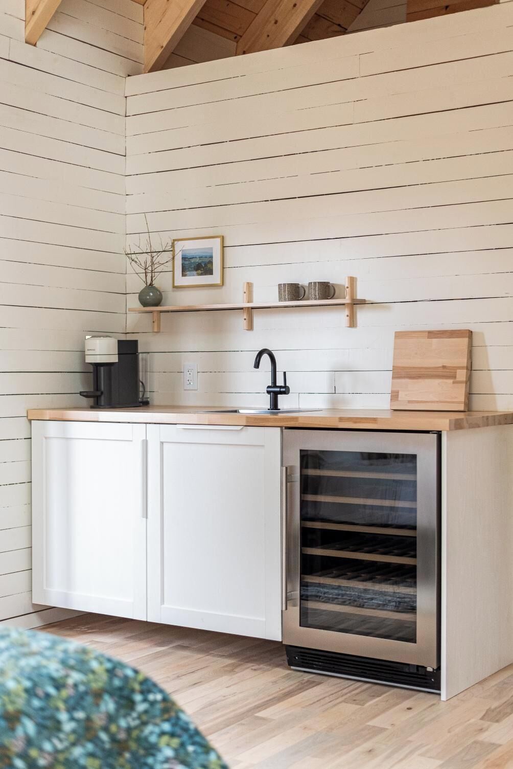A compact kitchen with white cabinets, a built-in oven, a coffee maker, and a shelf with mugs.