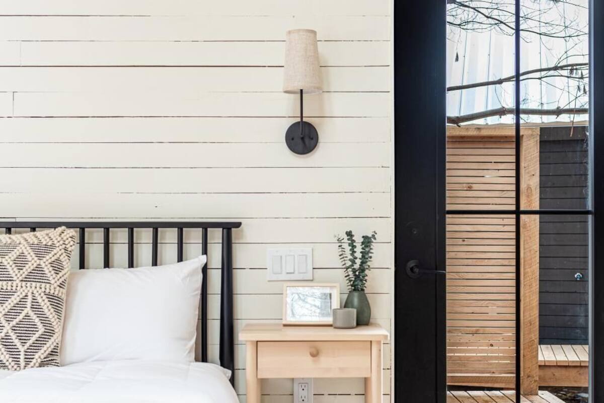 A bedroom with a bed, bedside table, lamp, and a view through a door.