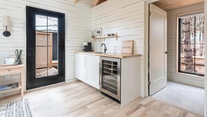 Cocina compacta con muebles blancos, horno empotrado y ventana con vista a una terraza de madera.