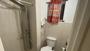 A bathroom with a shower, toilet, sink, and a window with a curtain.