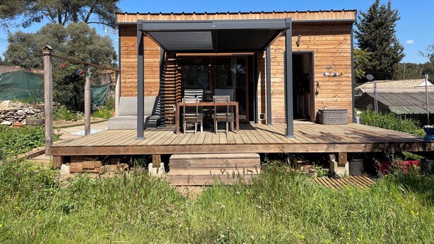 Eine moderne Holzhütte mit überdachter Terrasse, Sitzgelegenheit im Freien und Blick auf den umliegenden Wald.