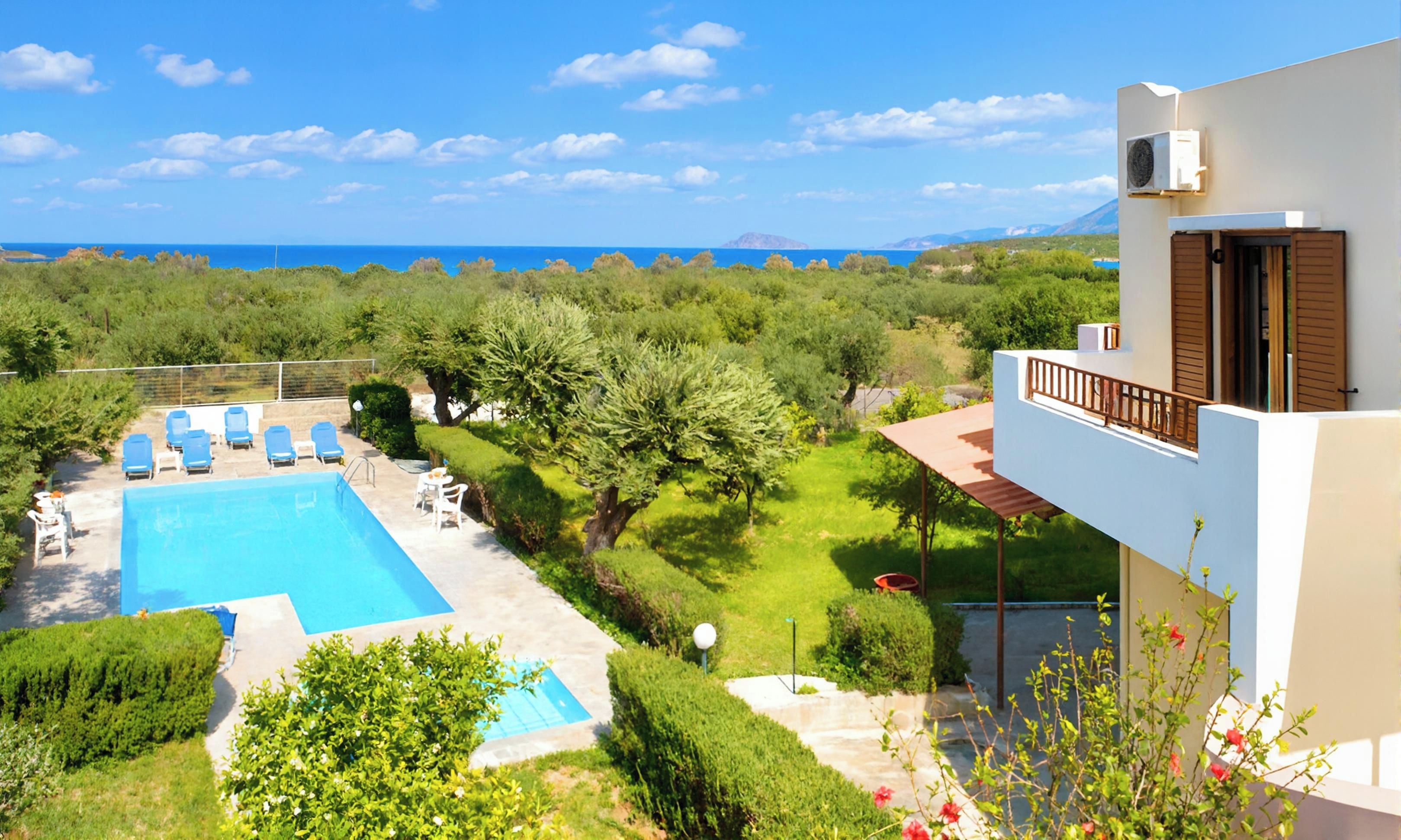A pool with lounge chairs, a garden, and a view of the sea.