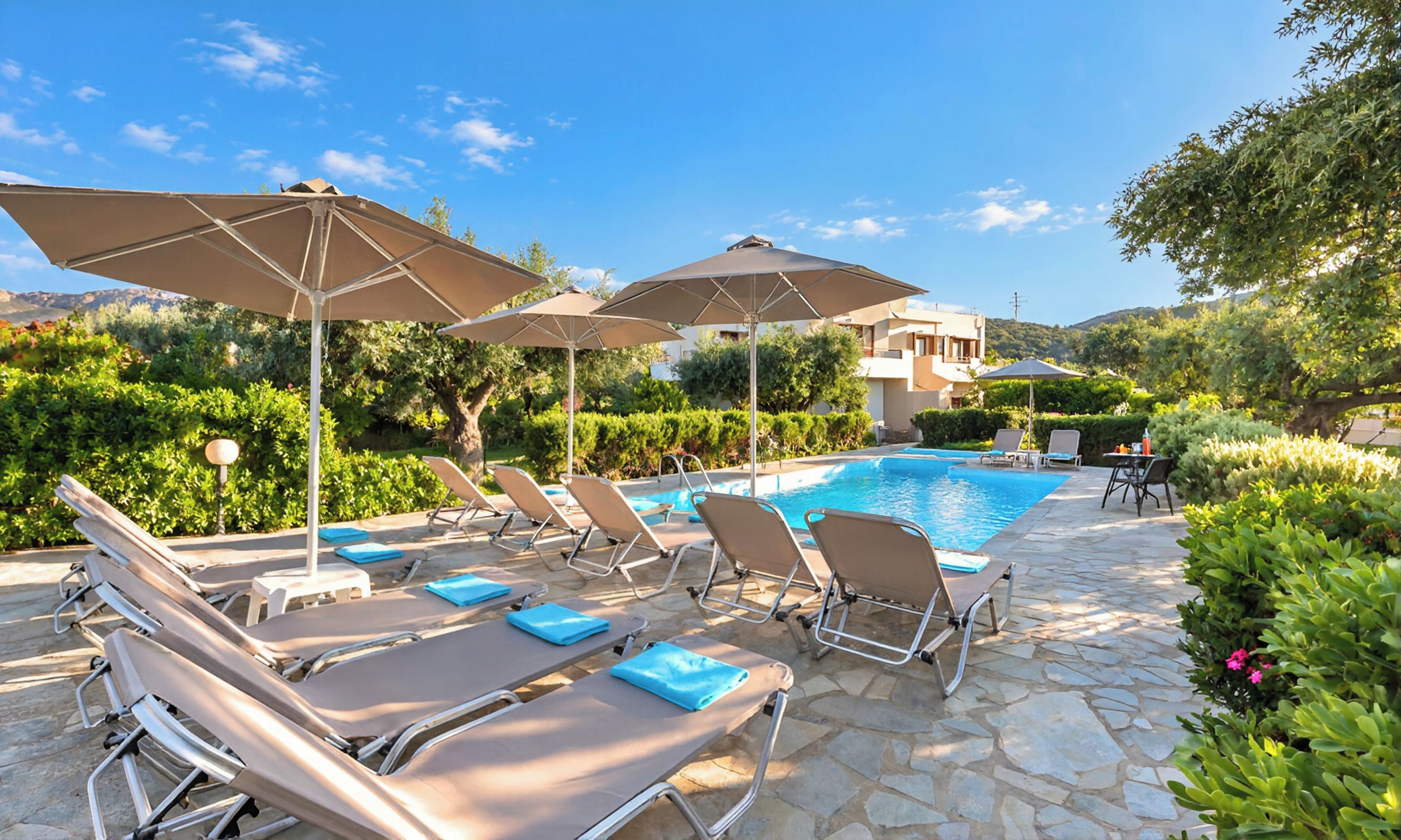A poolside area with lounge chairs and umbrellas, a clear blue sky, and a building in the background.