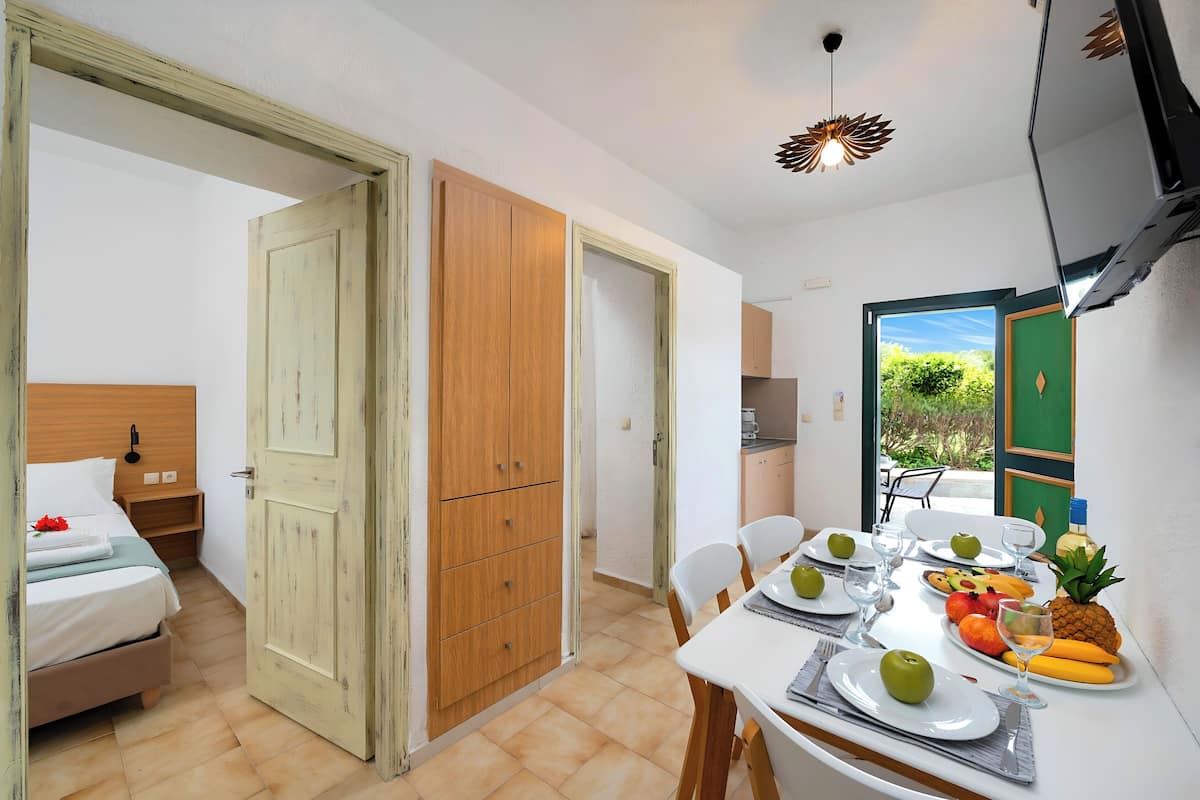 A room with a bed, wooden wardrobe, dining table with plates, glasses, and fruit.