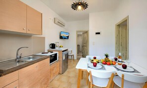 A compact kitchen with a sink, stove, and a dining area with a table set for two. - Plaisir Beachside Apts (Agios Nikolaos)